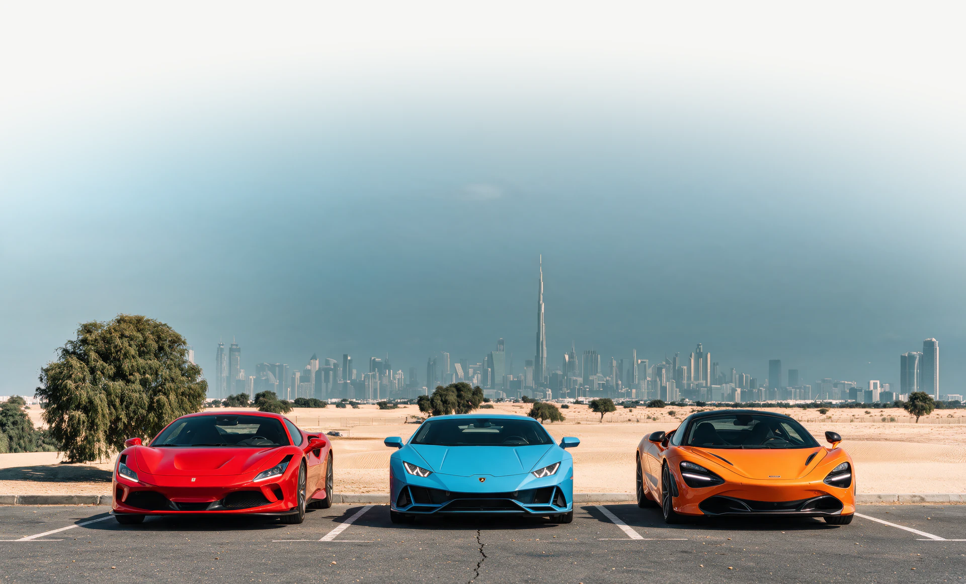 سيارة Ferrari F8 حمراء، وسيارة Lamborghini Huracán زرقاء وسيارة McLaren 720S برتقالية متوقفة أمام أفق دبي